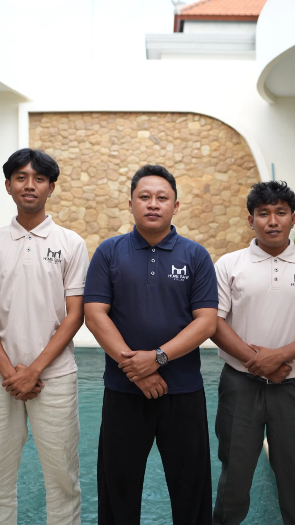 Three Homesafe Villas team members in branded uniforms standing beside the pool