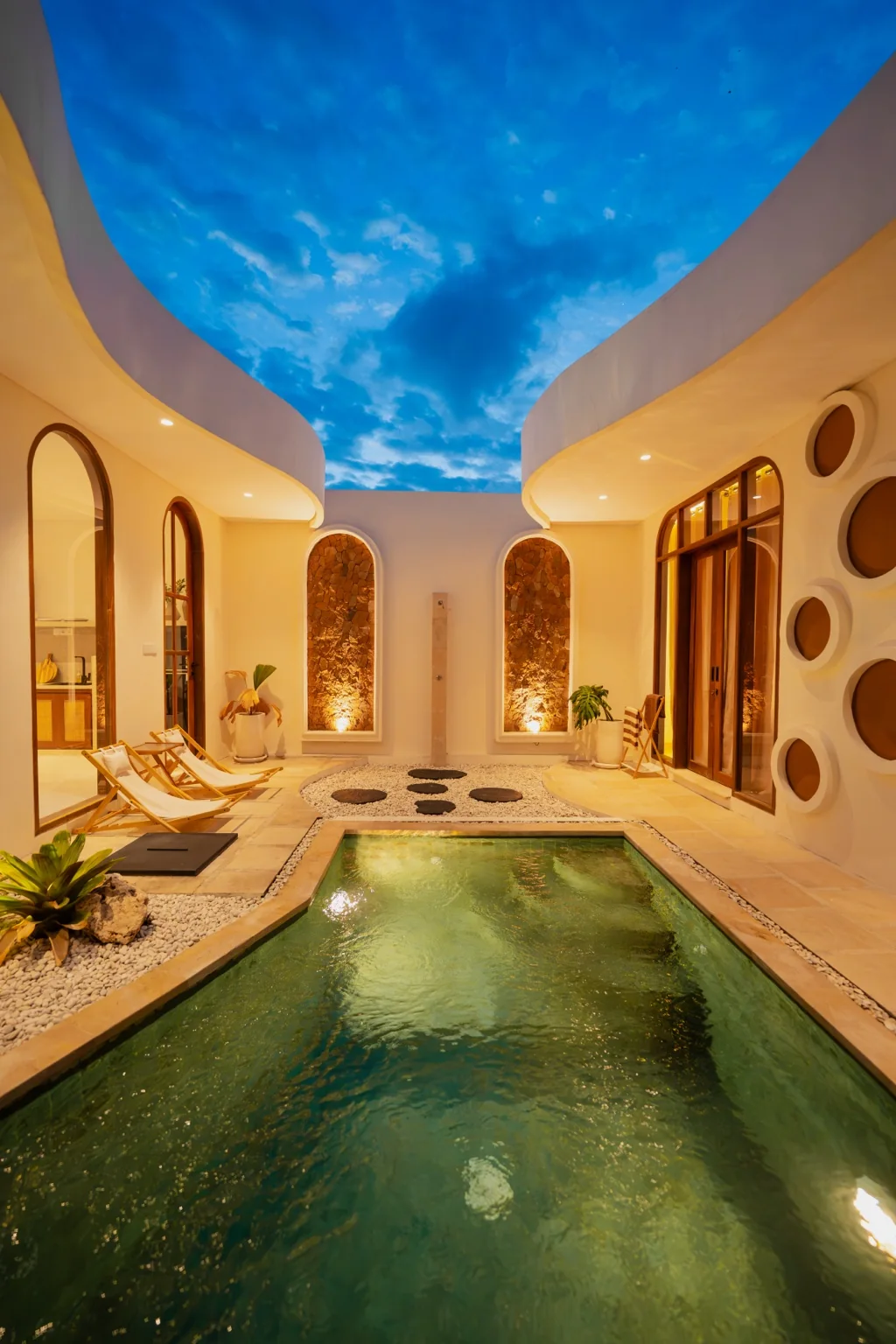 Private pool courtyard at Homesafe Villas at dusk, with illuminated stone niches and arched doors